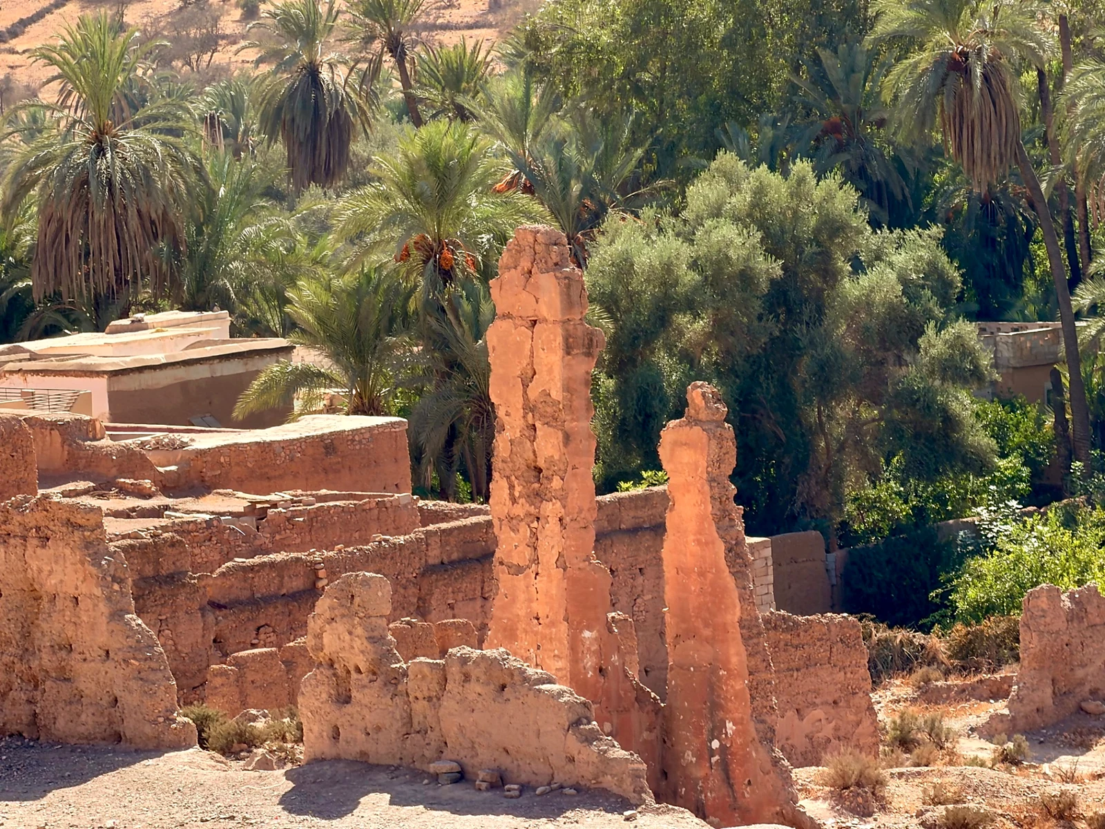 Broken earthen walls and tall remaining fragments of ruins behind Tiout kasbah