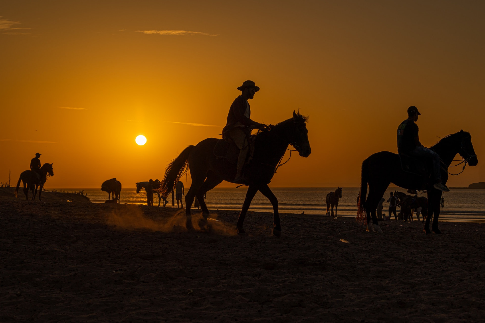Riders on horseback silhouetted along a Moroccan Atlantic beach at sunset