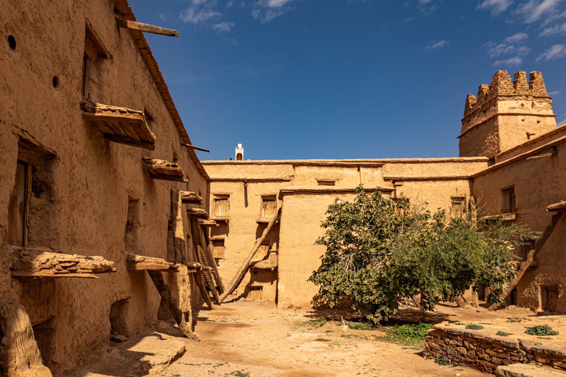 The earthen interior courtyard of the Aït Kine collective granary, with wooden support beams and a small tree