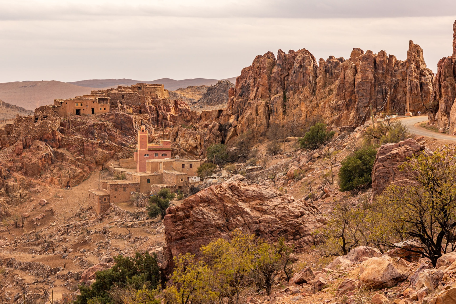 A small village and pink mosque minaret set among jagged red rock formations in the Anti-Atlas