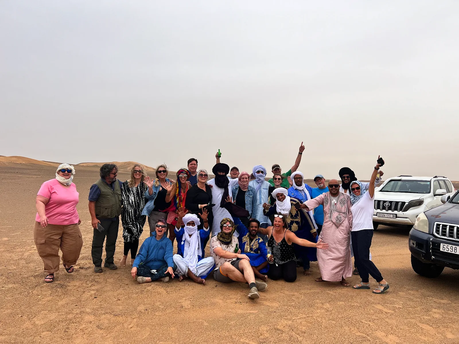 A private group of travellers in desert robes and headscarves celebrating together on a sandy plain near their 4x4 vehicles