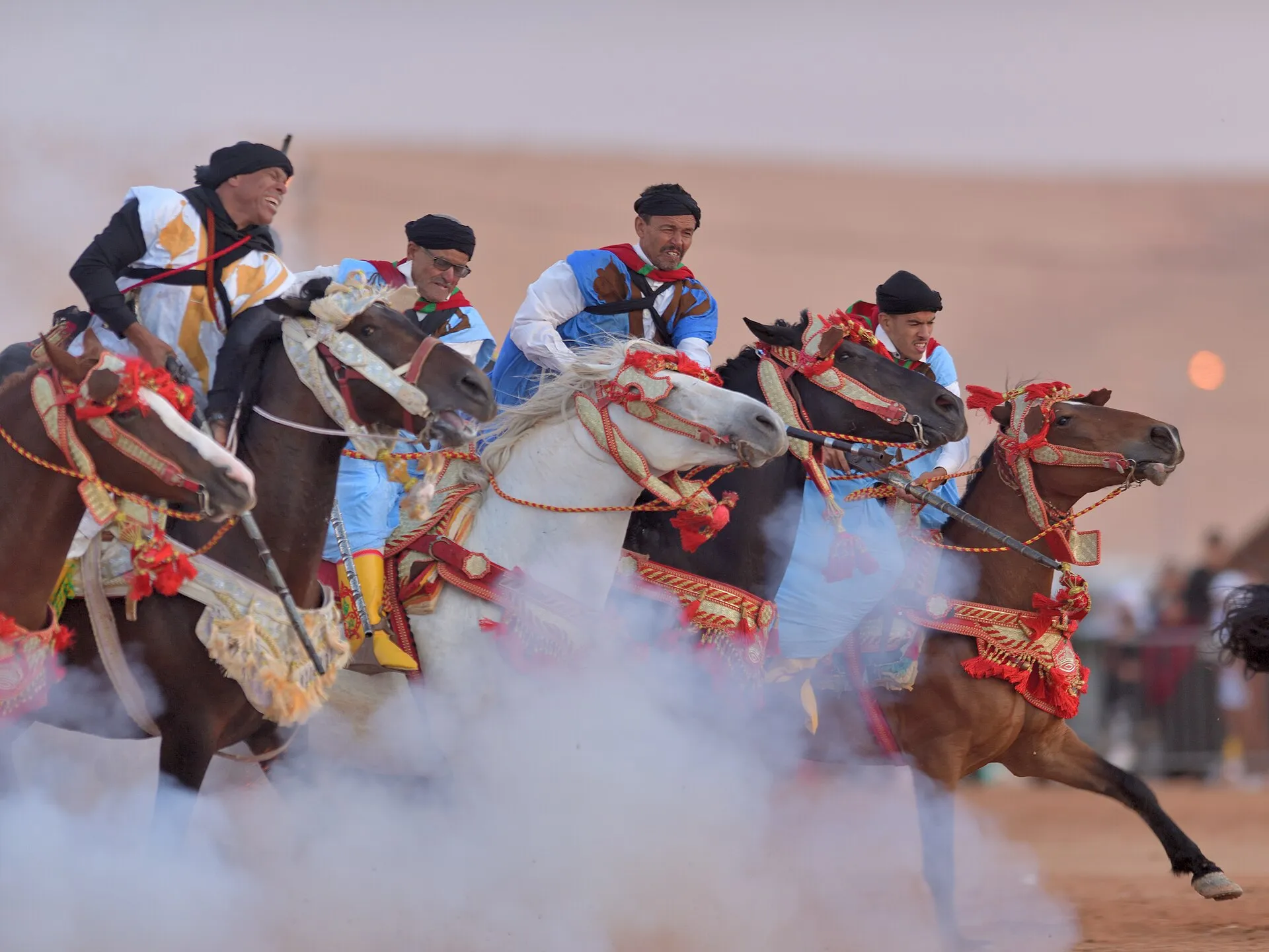 Tbourida horsemen in white and blue robes galloping as their muskets fire at the Tan-Tan Moussem