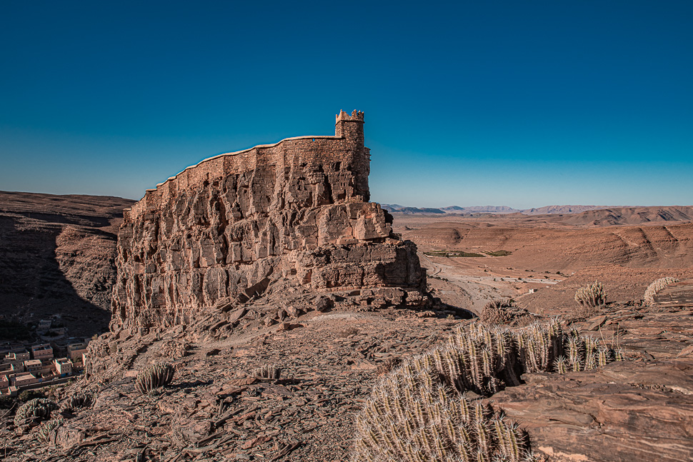 A stone collective granary built onto a rocky cliff above a dry valley in the Anti-Atlas