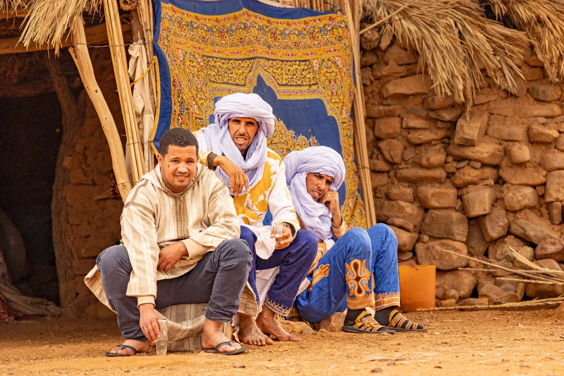 Three Moroccan men seated beside a traditional shelter in southern Morocco