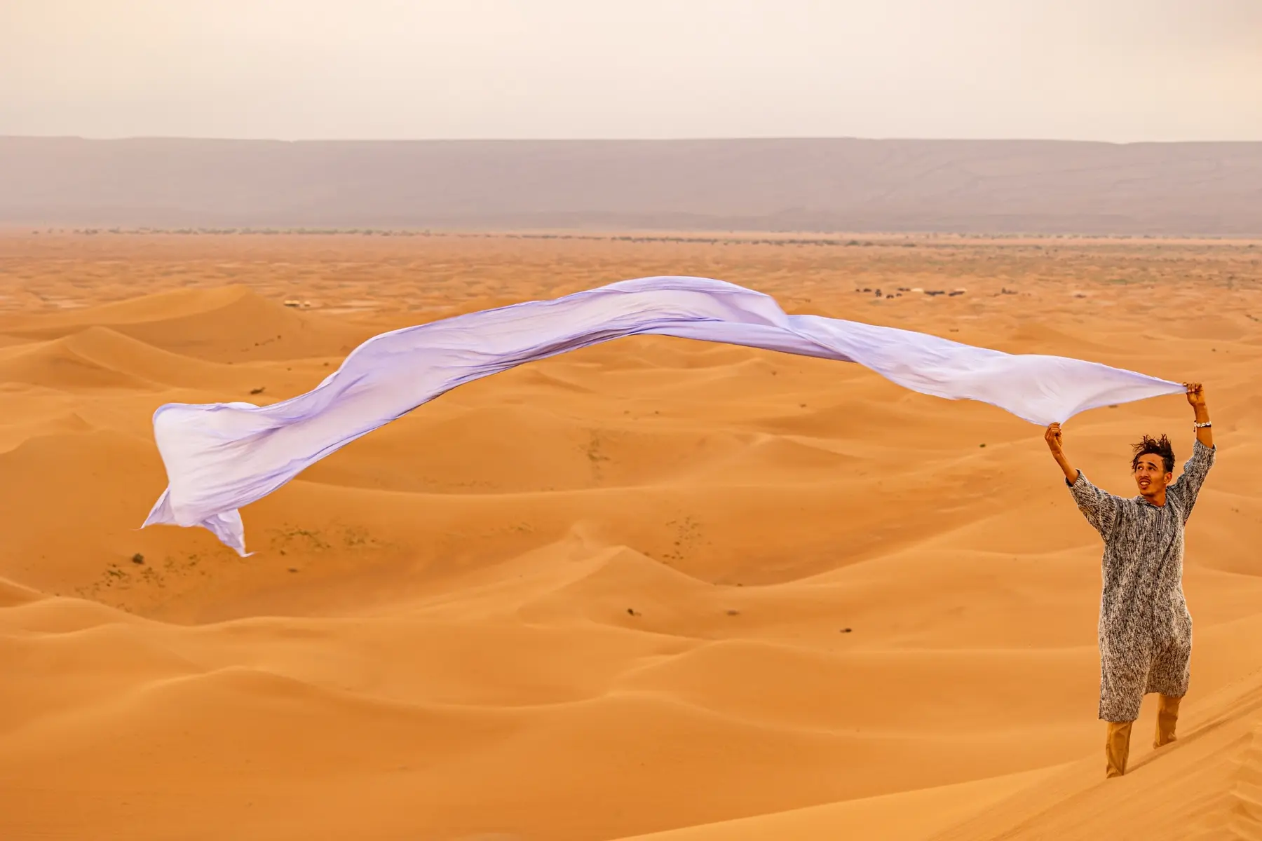 Young man holding flowing fabric above the dunes of Morocco’s Sahara